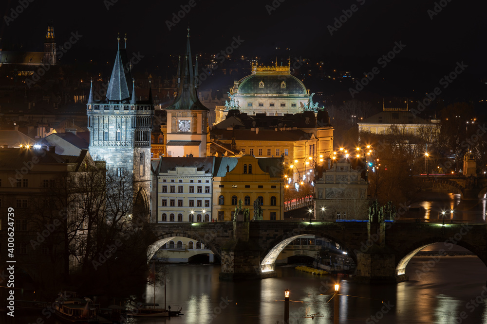 .old stone charles bridge and bridge tower on vltava river and light from street light in and roofs of surrounding buildings of prague city center at night