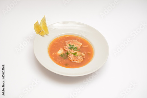 Tomato meat soup in a white plate on a white plate. Decorated with two lemon wedges. Can be used in the restaurant menu.