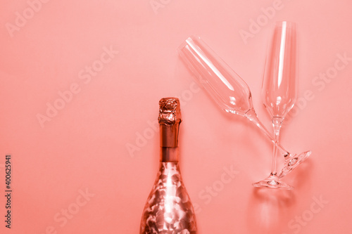 Bottle of champagne or sparkling wine with a couple of glasses on pink background.