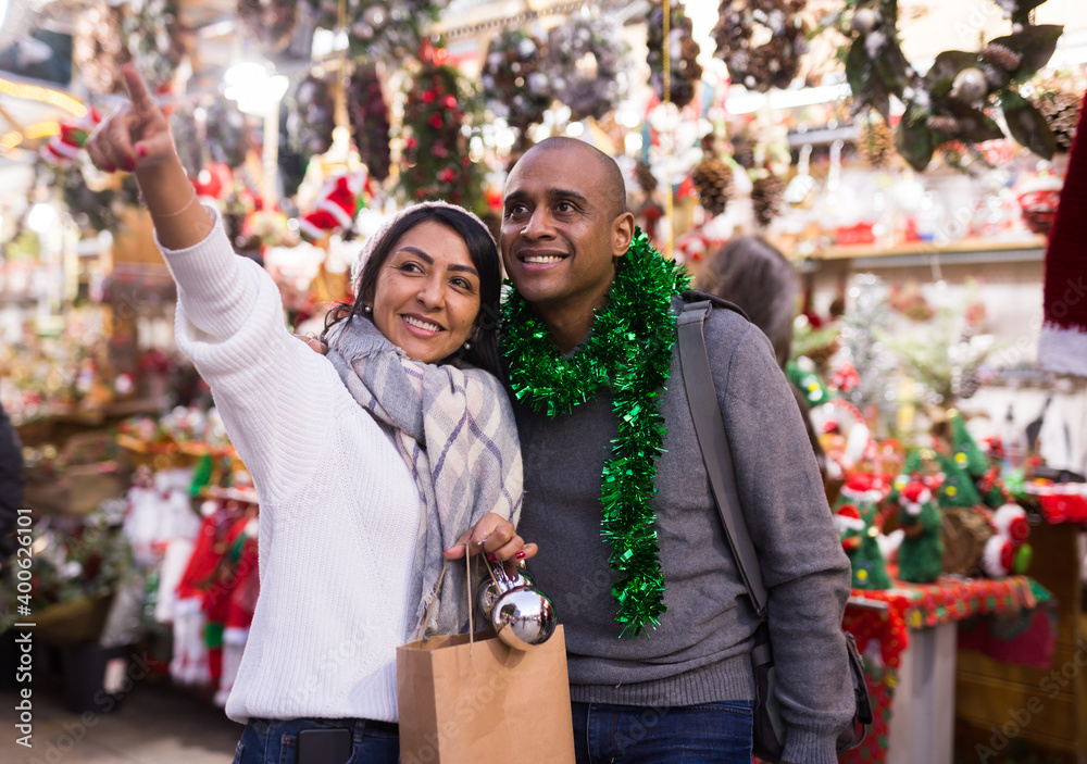 Cheerful married couple looking for decorations on Christmas street market while shopping