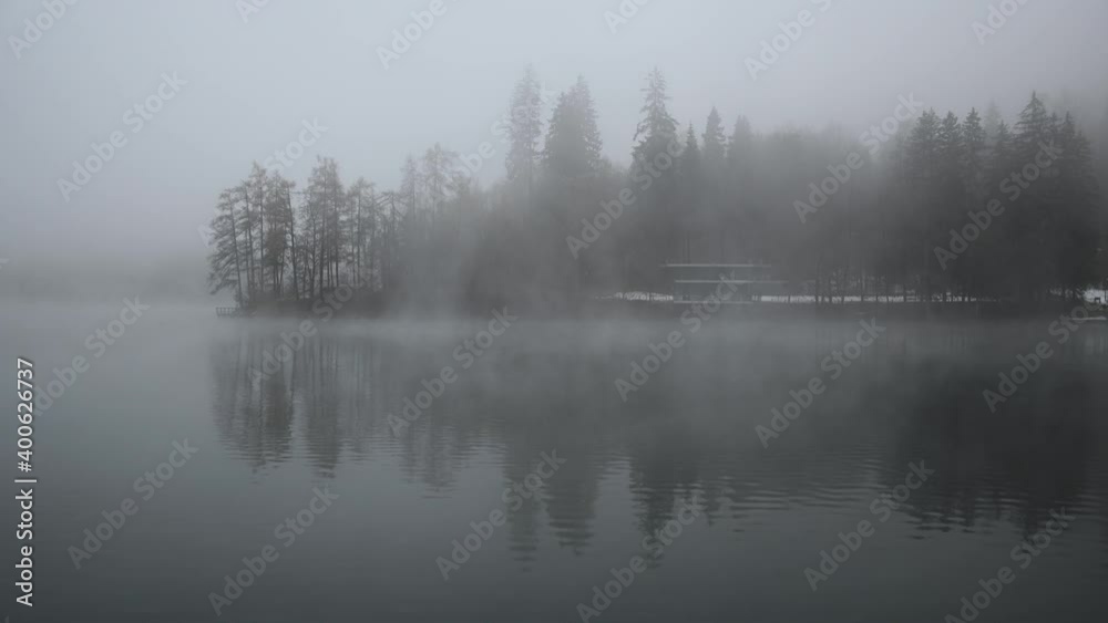 Fog slowly moving over lake Bled water, Slovenia. Surface covered with mist on winter cloudy day. Trees on glacial lake shore. Static shot, real time, wide angle Fog slowly moving over lake Bled water, Slovenia. Surface covered with mist on winter cloudy day. Trees on glacial lake shore. Static shot, real time, wide angle