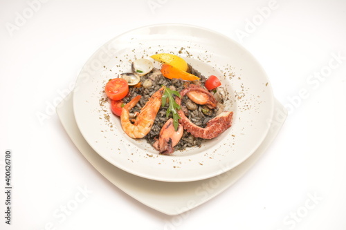 Risotto with seafood and cuttlefish ink on a white plate. Decorated with boiled shrimp and lemon wedges. Located on a white background. Can be used in the restaurant menu.