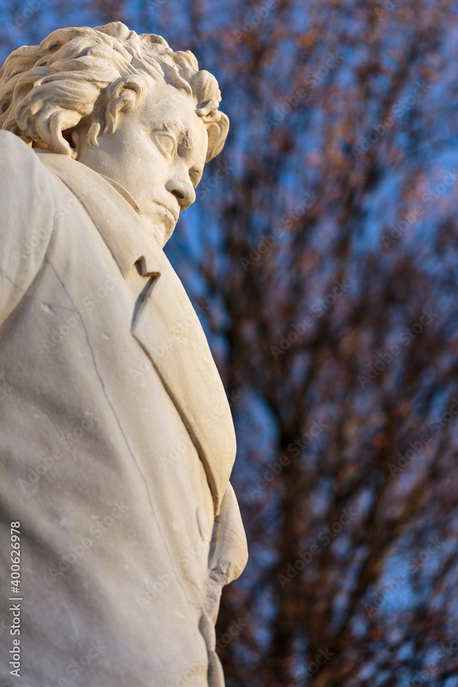 Obraz premium Stone figure of musical genius, composer and pianist Ludwig van Beethoven, in a monument from 1898. Vertical daylight view with blurry leafless trees in the background and blue sky