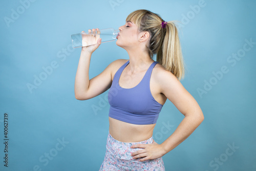 Young beautiful woman wearing sportswear holding a bottle of water over isolated blue background drinking water