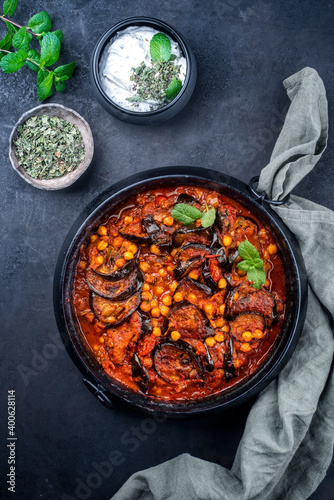 Modern style slow cooked Lebanese vegetarian eggplant stew maghmour served with chickpeas and yoghurt as top view in a design pot with copy space photo