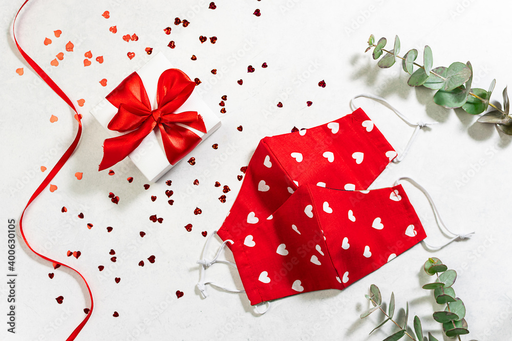 Fototapeta premium St. Valentine’s Day in pandemic time concept. Gift box, shining decorations and red protective masks on white marble background. Lockdown and holidays concept.