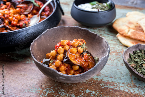 Modern style slow cooked Lebanese vegetarian eggplant stew maghmour served with chickpeas and pita bread as close-up in a rustic design bowl photo