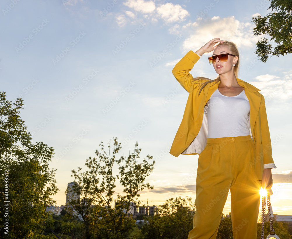 Beautiful blonde woman in a yellow fashionable trouser suit on the background of the blue sky and nature. Beautiful blonde woman in a yellow fashionable trouser suit on the background of the blue sky and nature.
