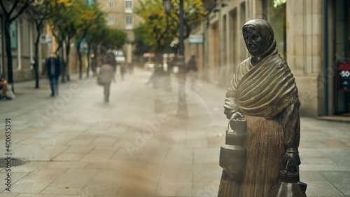 sculpture of a milkmaid from Ourense, with a trail of people and cars passing by. central street of ourense, with people passing by and sculpture. person walking through the limes of ourense.