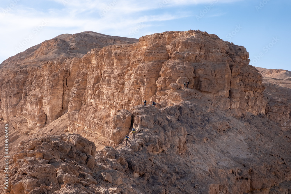 A group of hikers going along steep ridge. Hard and dangerous hiking trail. Extreme climbing and adrenaline. Amazing mountain landscape in Makhtesh Ramon, Negev desert, Israel
