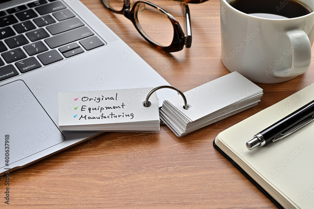 There's a laptop computer, a notebook, a pen and an open vocabulary book on the desk. The word Original Equipment Manufacturing is written on it.