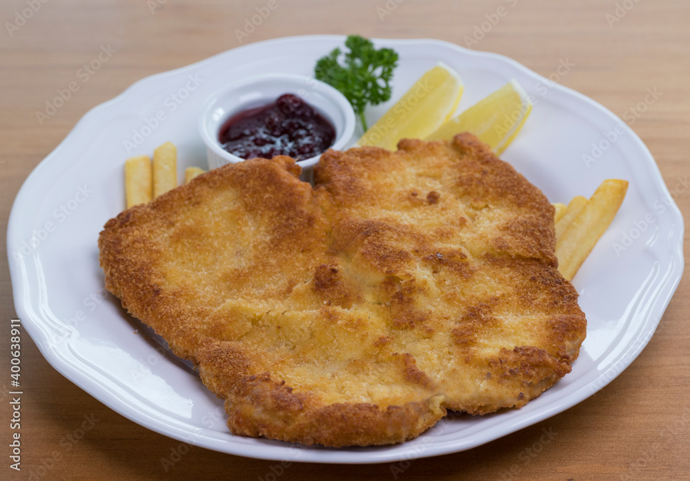 Crumbed pork escalope called Schnitzel served with French fries, cranberry sauce and lemon