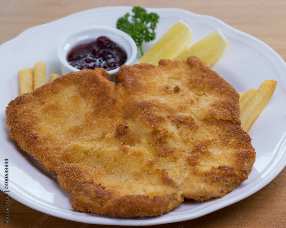 Crumbed pork escalope called Schnitzel served with French fries, cranberry sauce and lemon Crumbed pork escalope called Schnitzel served with French fries, cranberry sauce and lemon
