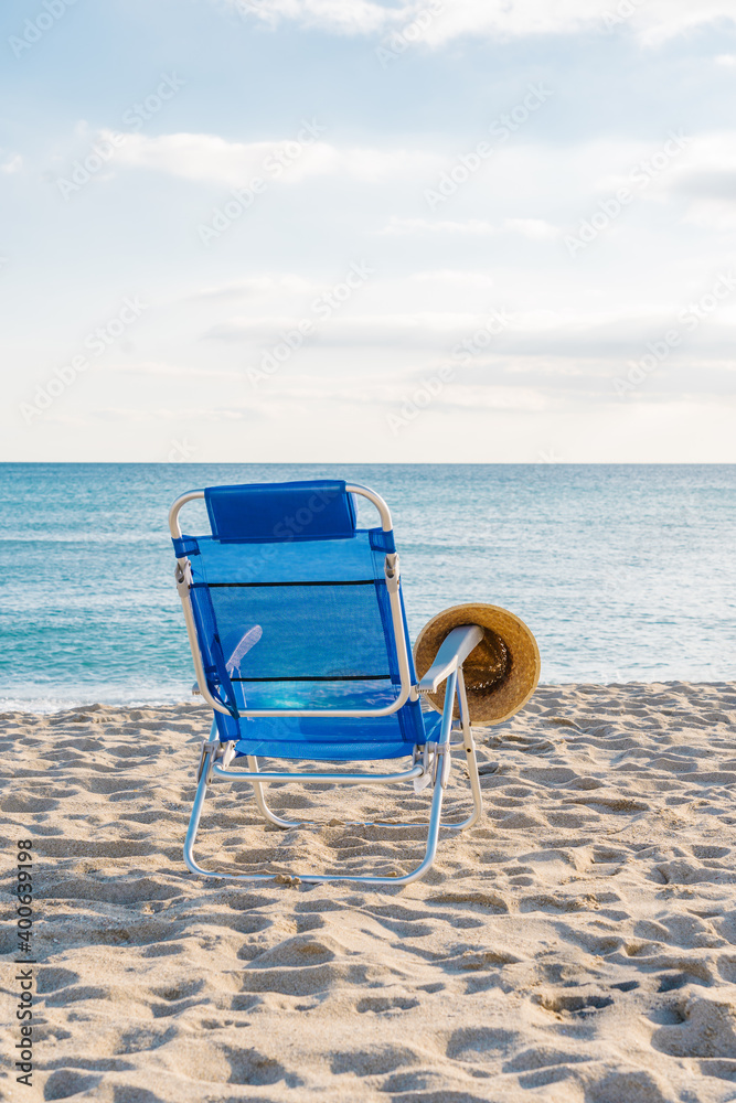 straw hat on top of a blue chair on a deserted beach straw hat on top of a blue chair on a deserted beach