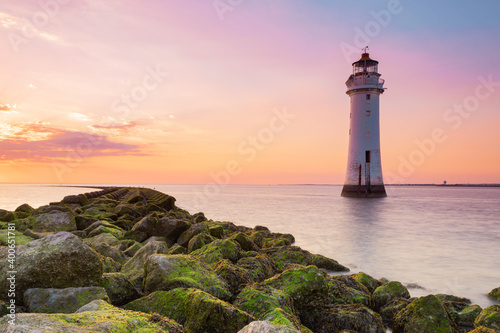 sunset time from a greenish rocks on a beach and a lighthouse at the background 