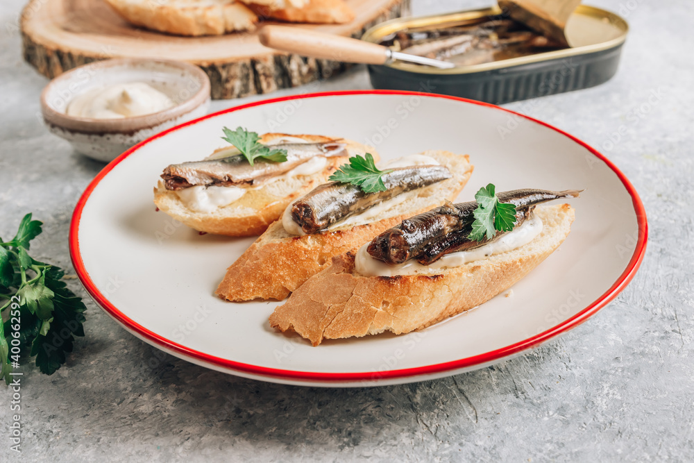 Homemade sandwich with sprats, sauce and parsley on white plate over gray background. Homemade sandwich with sprats, sauce and parsley on white plate over gray background.