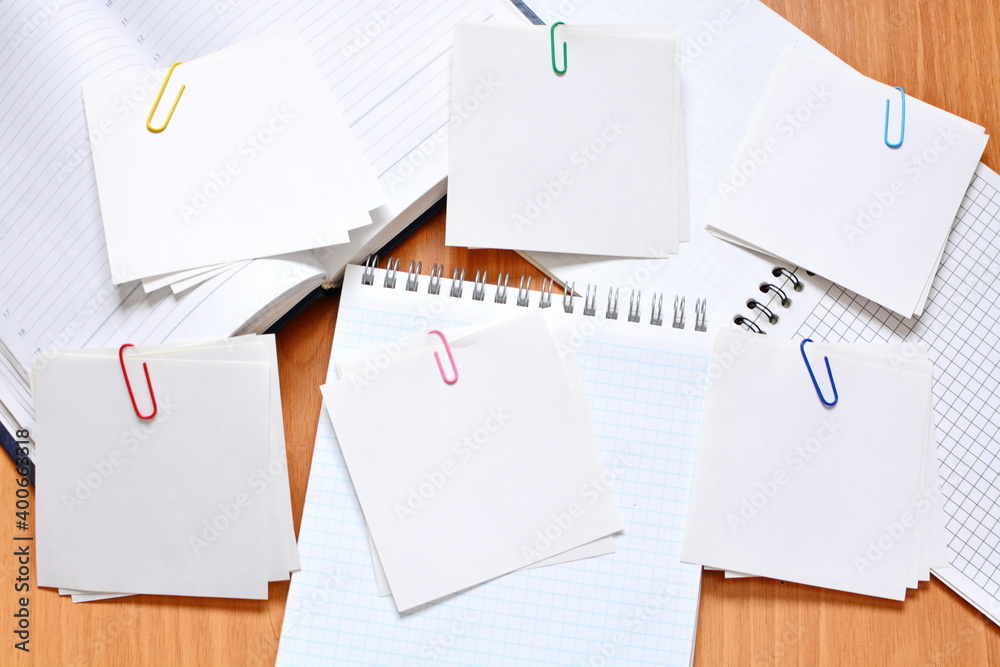 Several pieces of white blank sheets of note paper in groups held together with paper clips on notebooks and daily planner. Copy space Several pieces of white blank sheets of note paper in groups held together with paper clips on notebooks and daily planner. Copy space