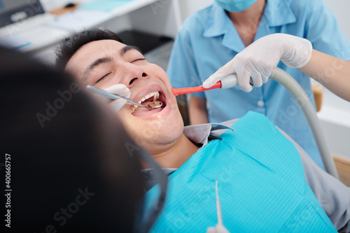 Dentist checking teeth of patient with mouth mirror when assistant putting in dental suction device