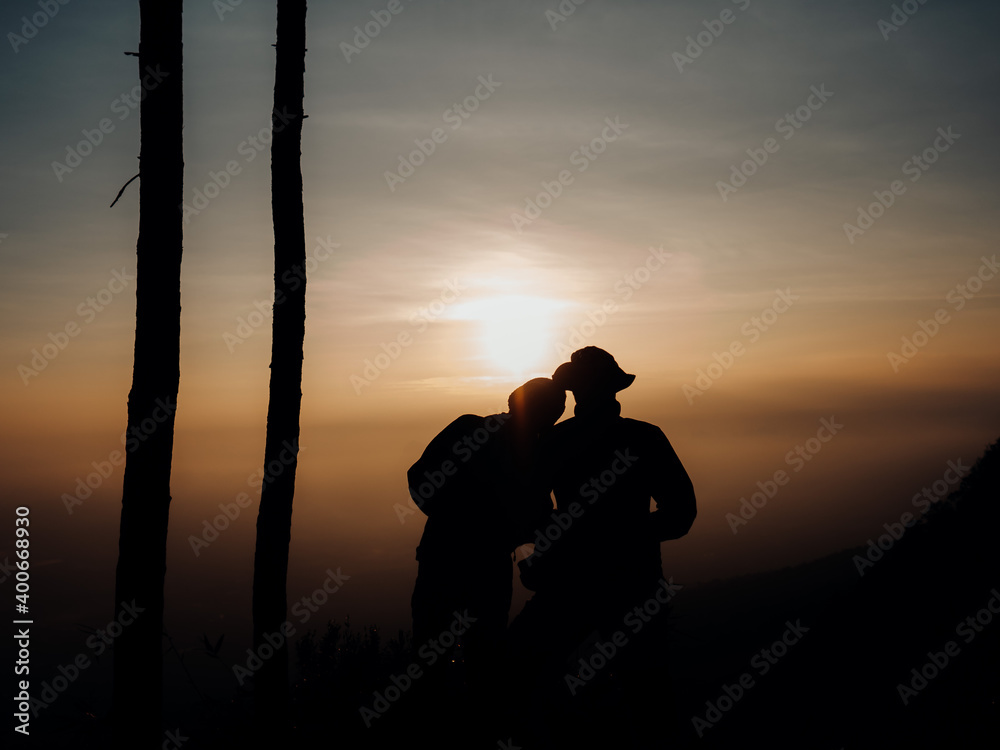 Two young tourists Silhouette, watching the sunrise at the edge of the cliff in the early morning. In the tourist season at Phu Kradueng National Park