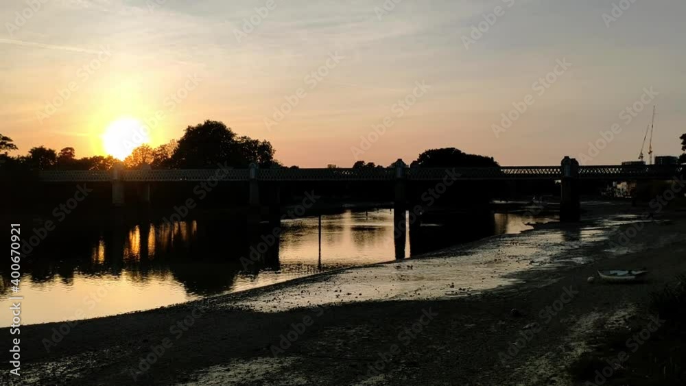 Beautiful sunset on Thames river, London. Kew Railway bridge can be seen on the picture and three people on Stand Up Paddle boards paddling on the distance. Beautiful sunset on Thames river, London. Kew Railway bridge can be seen on the picture and three people on Stand Up Paddle boards paddling on the distance.