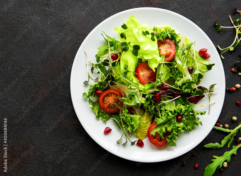 Fresh green mixed  salad bowl with tomatoes and microgreens  on black concrete background. Healthy food, top view.