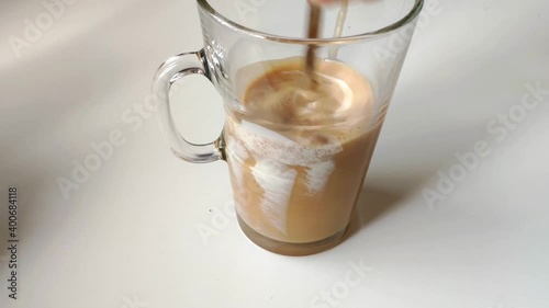 Making an Irish coffee. Transparent glass filled half way with black coffee and cream recently poured. A spoon is put inside and is all stirred. photo