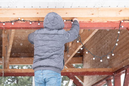 Young man decorating house with Christmas lights outdoors