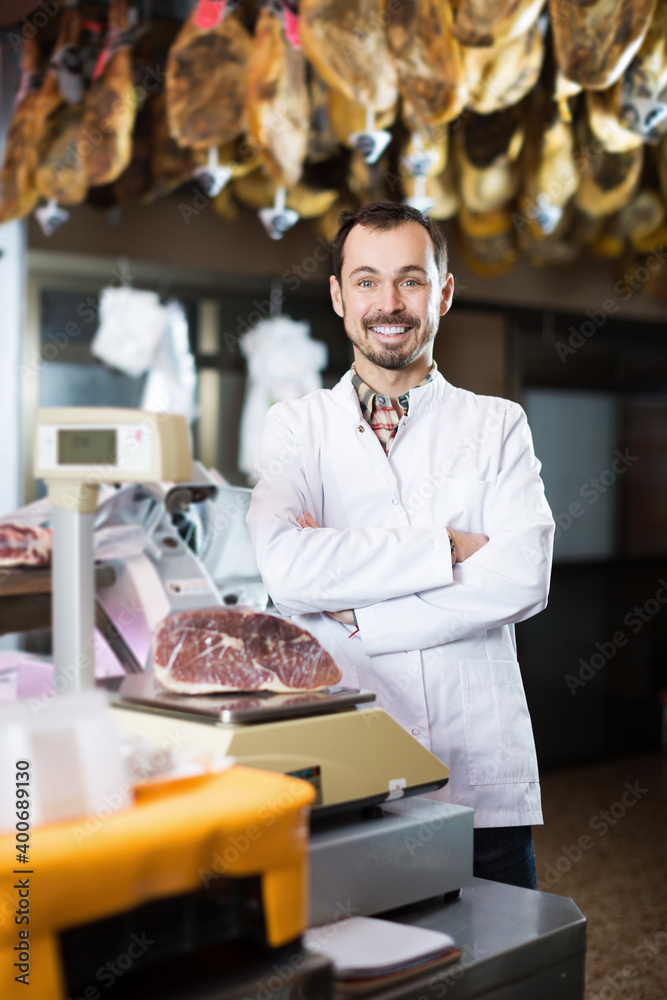 Positive male assistant using scales in butcher shop