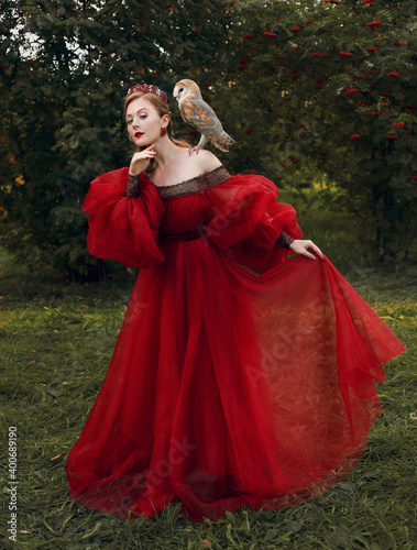 Tender woman in red medieval dress with owl on shoulder photo