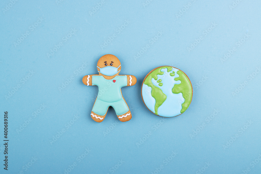 the gingerbread man is a doctor in medical mask and blue uniform with a gingerbread planet earth. the concept of a global coronavirus pandemic, thanks to the doctor