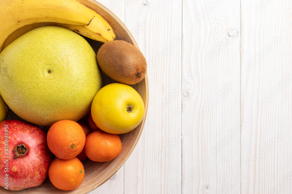 Wooden bowl with different fruits on white table. Top view, close up.
