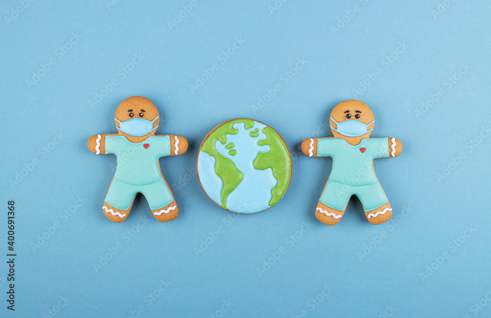two gingerbread man medics in a mask with the gingerbread planet earth on a blue background two gingerbread man medics in a mask with the gingerbread planet earth on a blue background
