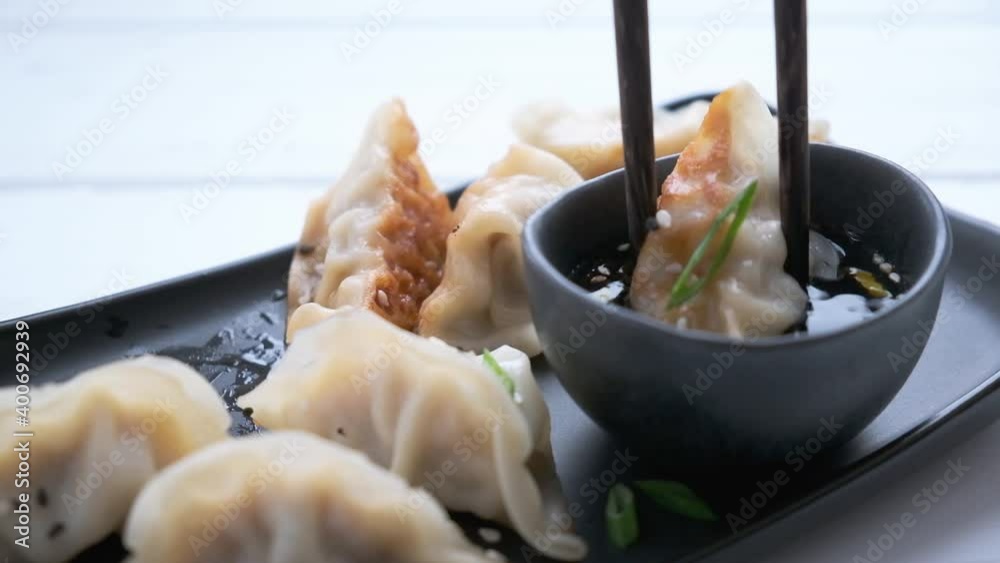 Fried gyoza dumplings with sauce and green onions on black plate, dark background. Japanese cuisine concept.