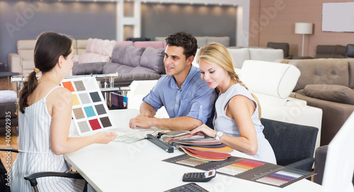 Couple who are consulting with the assistent about the choice of a color for new sofa