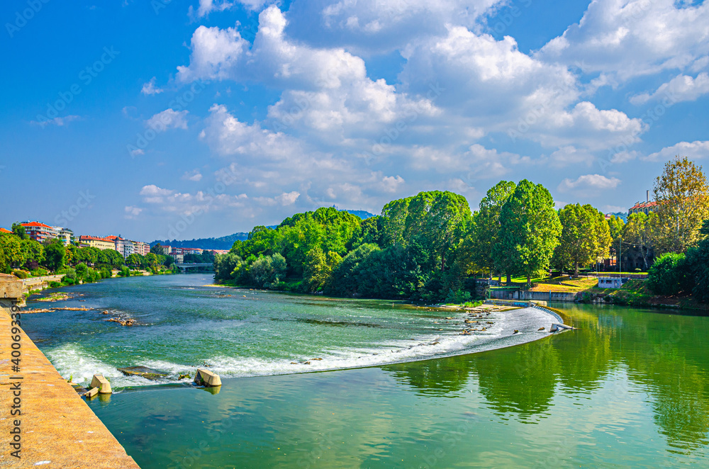 Po river in Turin city historical centre with water dam and green trees on shore, blue sky white clouds background, Piedmont, Northern Italy