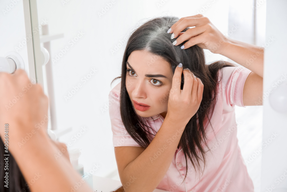 Fototapeta premium Stressed woman with graying hair looking in mirror