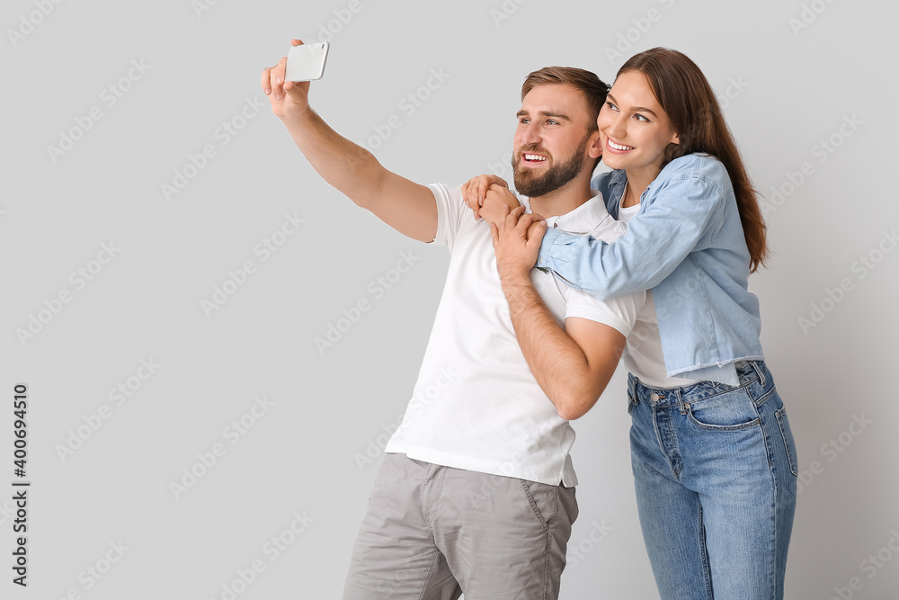 Fototapeta premium Young couple taking selfie on light background