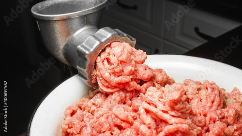 Meat grinder in action and ground beef meat. Horizontal close-up color image of process of grinding preparation of minced raw red meat in Grinder. photo