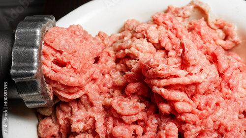 Meat grinder in action and ground beef meat. Horizontal close-up color image of process of grinding preparation of minced raw red meat in Grinder. photo