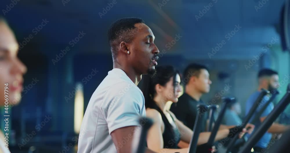 Modern gym concept. Active team of sportsmen and sportswomen working out cross trainers. Afro-american handsome fitness coach stops exercising and smiling. Modern gym concept. Active team of sportsmen and sportswomen working out cross trainers. Afro-american handsome fitness coach stops exercising and smiling.