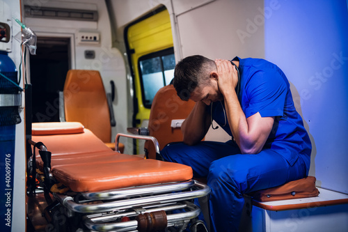 Fototapeta Overworked paramedic having a little break, massaging his nape in an ambulance car