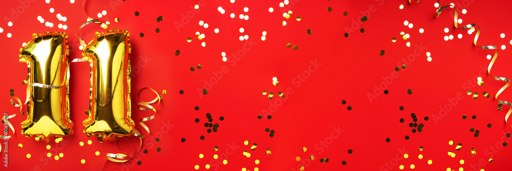 Fototapeta premium Gold foil balloon number, digit eleven. Birthday greeting card, inscription 11. Anniversary celebration event. Banner. Stylish golden numeral, light bokeh, glitter, red background. Numerical digit