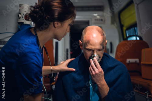 An injured man pressing an oxygen mask to his face, a female paramedic is trying to calm him down.