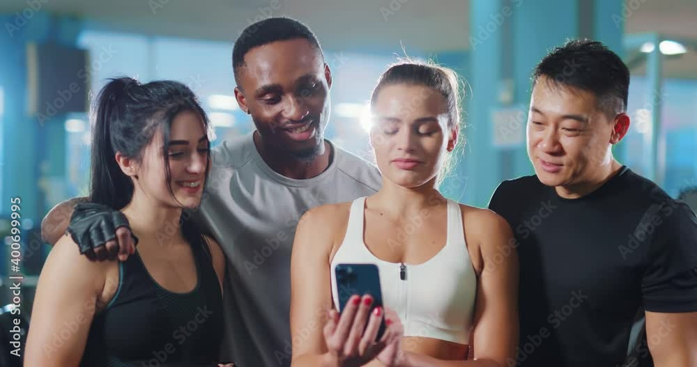 Attractive athletic group of friendly young attractive people using smartphone together after intense team workout training in the gym. Attractive athletic group of friendly young attractive people using smartphone together after intense team workout training in the gym.