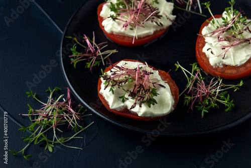 Black plate with tomato slices with cream and watercress microgreens on dark textured background