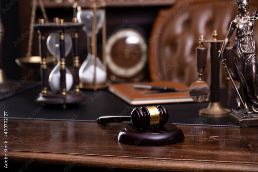 Law and justice theme. Judge chamber. Themis statue, gavel and scale on brown desk. Legal books in the bookshelf as background. Law and justice theme. Judge chamber. Themis statue, gavel and scale on brown desk. Legal books in the bookshelf as background.