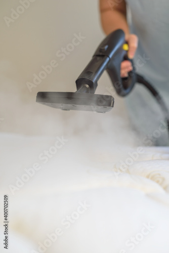 Woman with steam generator cleans bed. Vertical photo