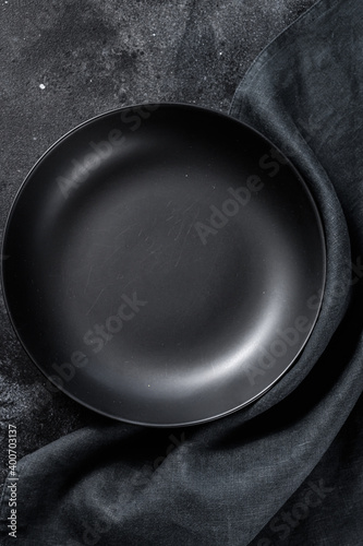 Black plate and a towel on textured black background.  Top view. Copy space