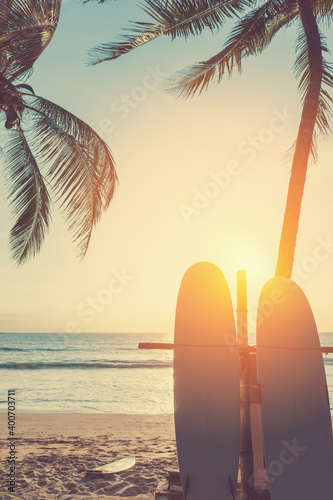 Surfboard and palm tree on tropical sunset beach with sun light abstract background. Summer vacation and sport extreme concept.