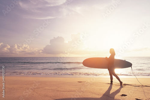 Woman hold surfboard standing at tropical sunset beach background. Summer vacation and sport adventrue concept.